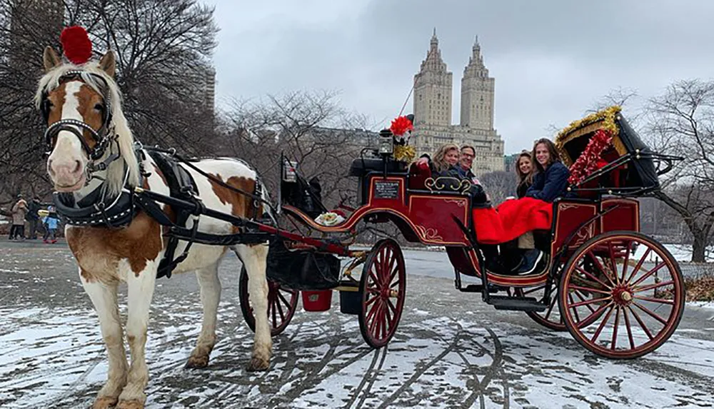 A horse-drawn carriage carries cheerful passengers through a snowy park with an iconic building in the background