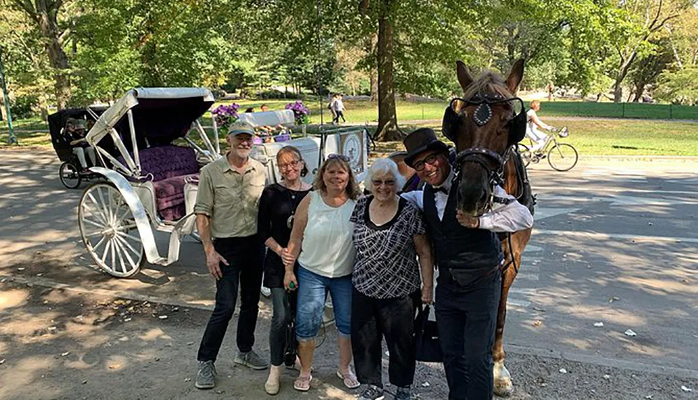A group of people is posing for a photo with a horse and carriage likely in a park setting with one person holding the horse by the bridle