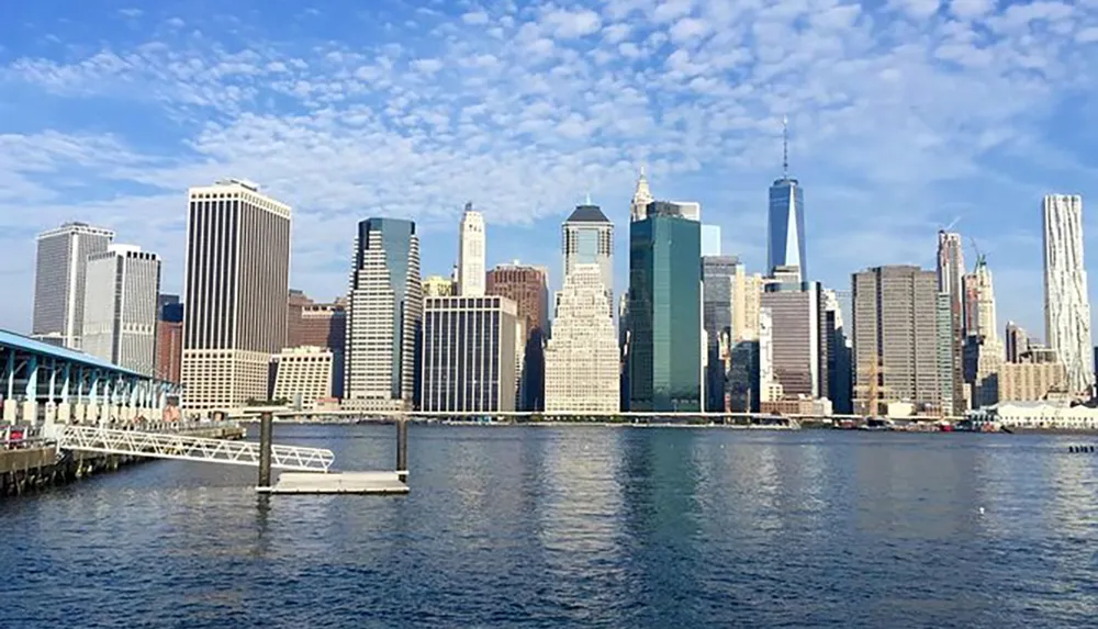 The image showcases a sunny panoramic view of Lower Manhattans skyline as seen from across the water featuring the distinctive One World Trade Center standing tall among other skyscrapers