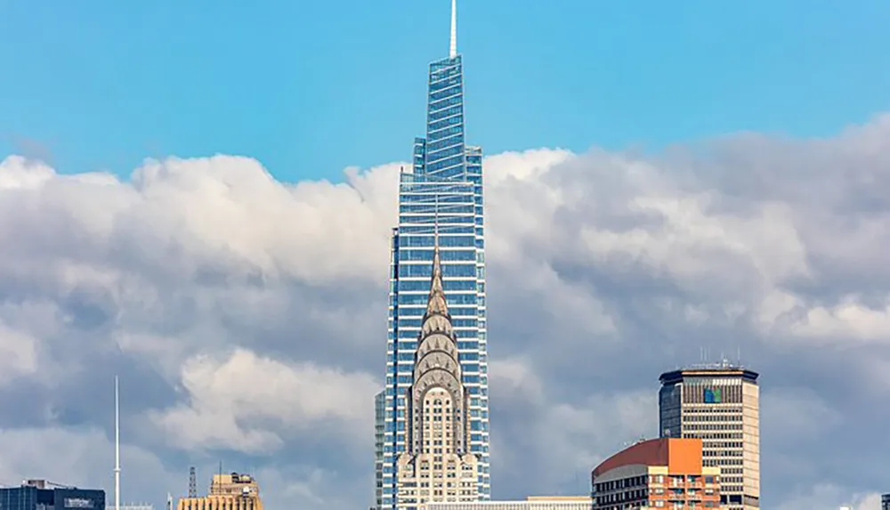 The image shows a tall modern skyscraper towering over other buildings against a backdrop of fluffy white clouds in a blue sky