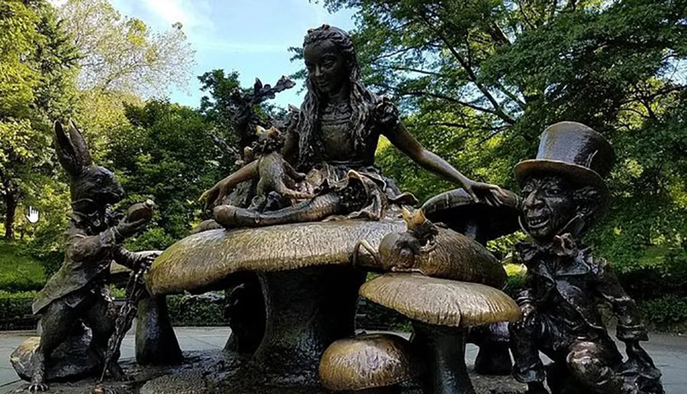 The image shows a bronze statue depicting characters from Alice in Wonderland with Alice seated at a mushroom table surrounded by The Mad Hatter The March Hare and other fanciful creatures in a park setting