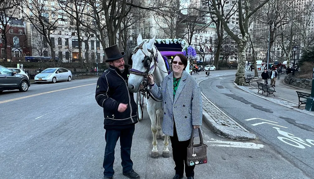 A person wearing a top hat stands beside a white horse while another individual smiles next to them in an urban park setting