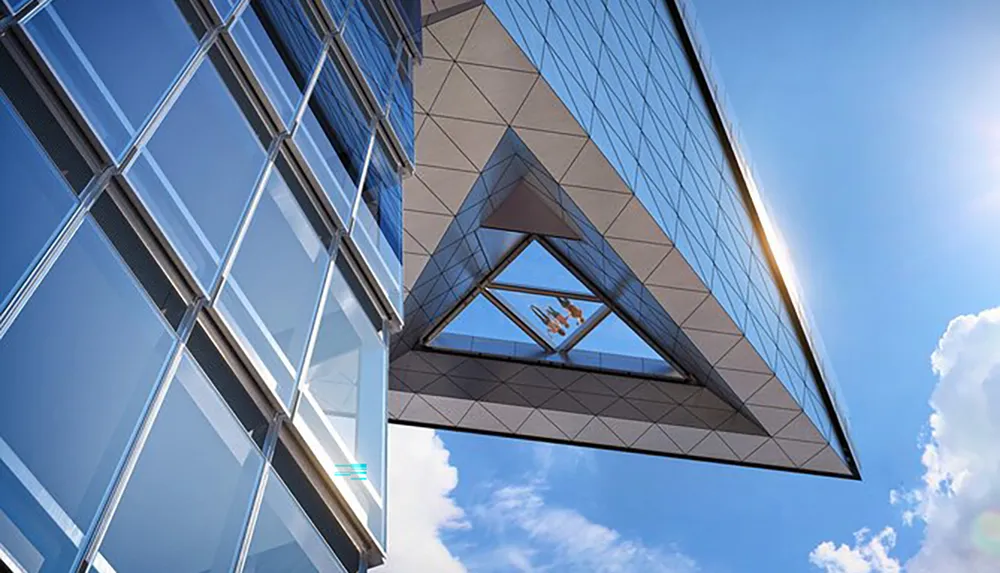 The image shows a modern building with geometric glass facades under a clear blue sky featuring a large triangular overhang with a window that frames a person lounging inside
