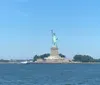 The image shows the Statue of Liberty standing on Liberty Island viewed from the water against a clear blue sky