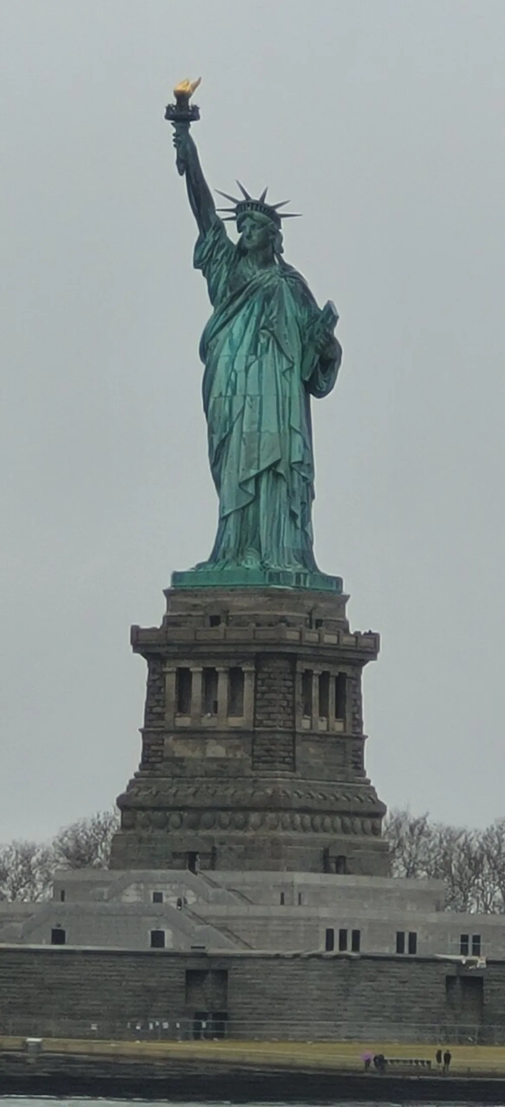 This image shows the Statue of Liberty standing tall against a cloudy sky
