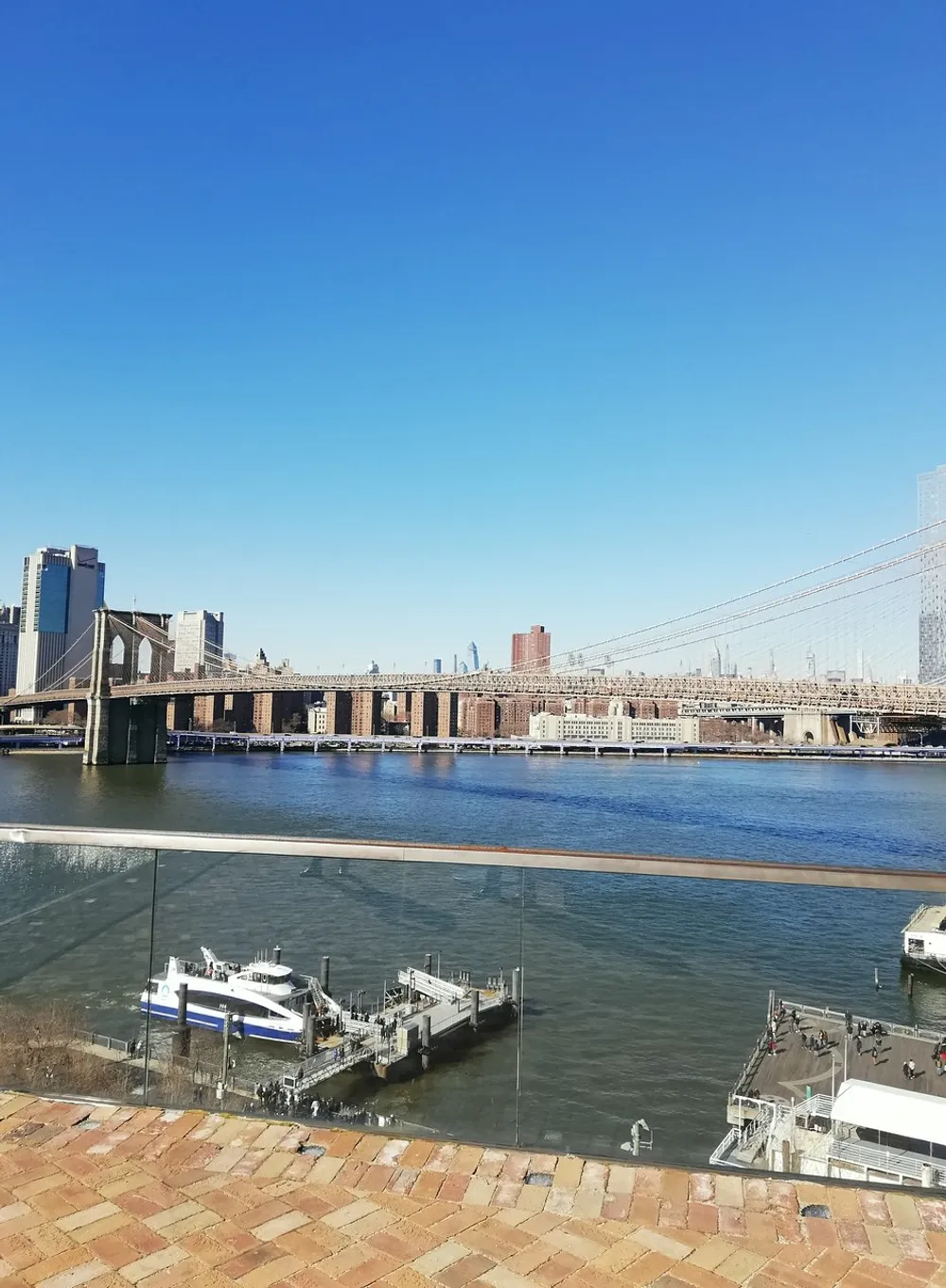 This image captures a sunny day view of a bridge over a river with docked boats and a city skyline in the background