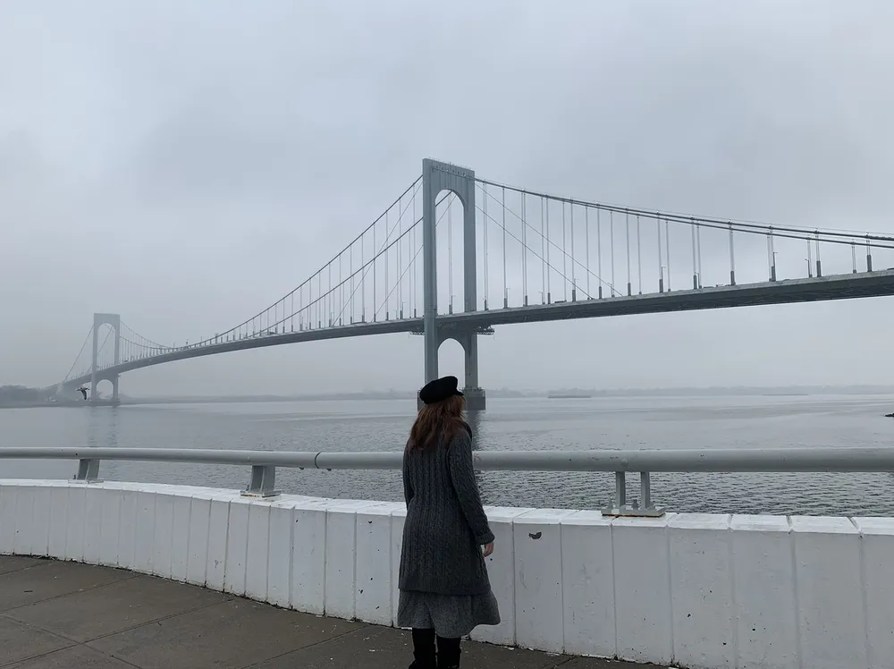 A person is gazing out at a foggy suspension bridge over a body of water
