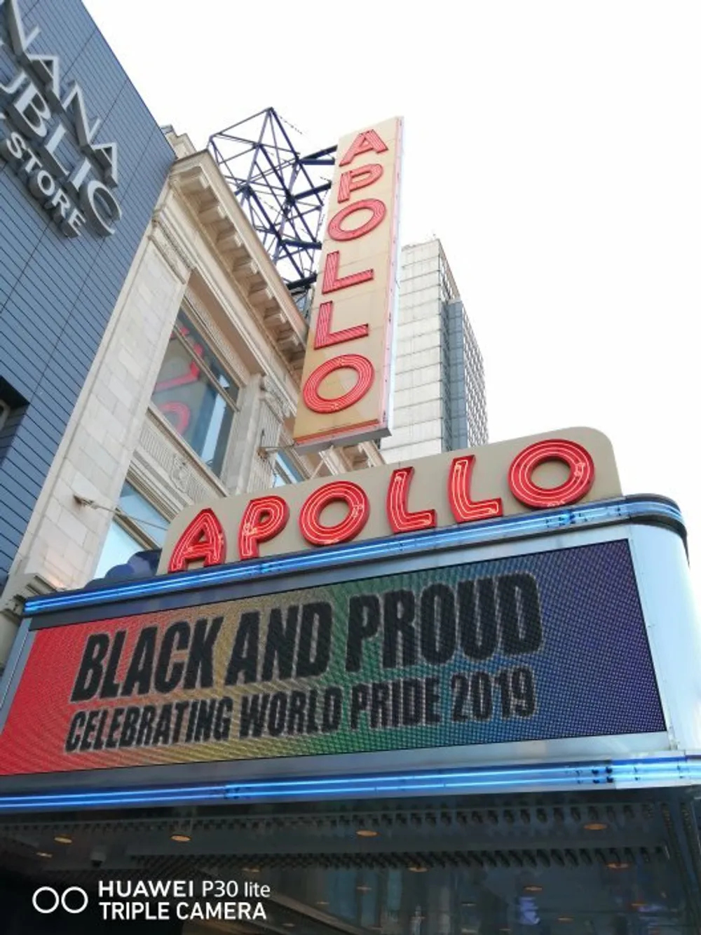 The image captures the iconic Apollo Theater marquee displaying a message BLACK AND PROUD CELEBRATING WORLD PRIDE 2019