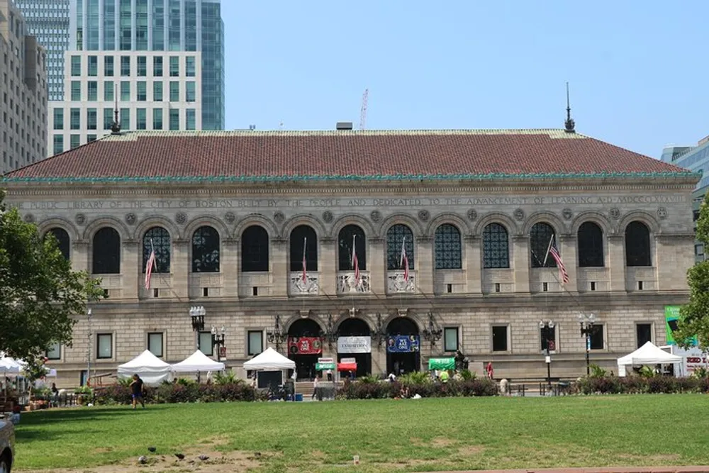 The image shows a stately building with arched windows and flags set against a clear sky with some trees and tents in front suggesting a public or historical venue possibly a library or government edifice