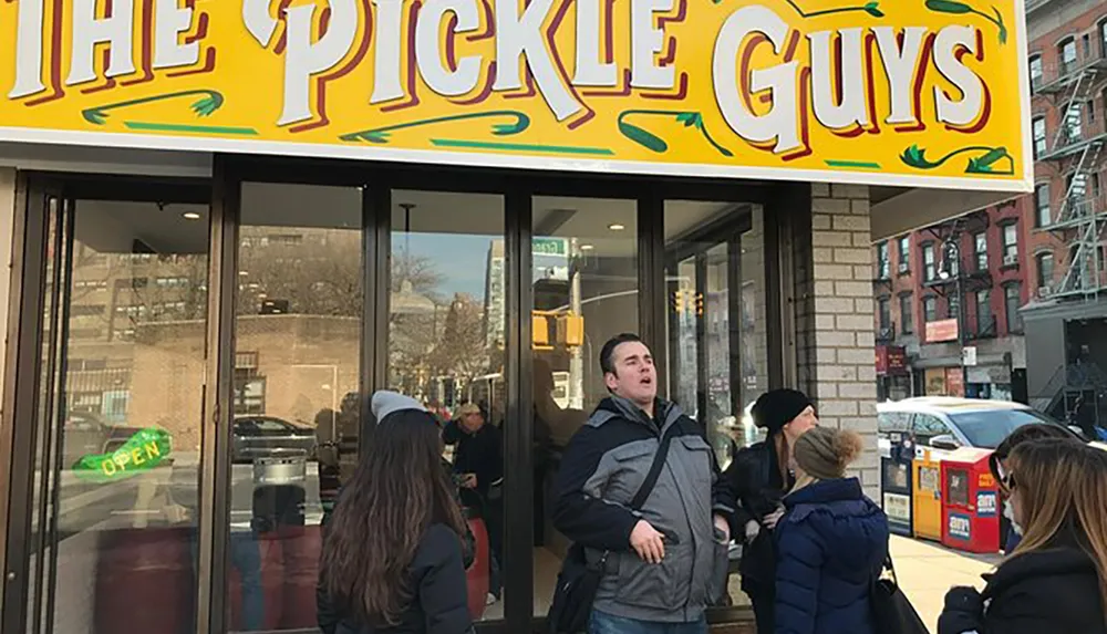 People are standing in front of a store named The Pickle Guys suggesting a bustling scene possibly indicative of the stores popularity