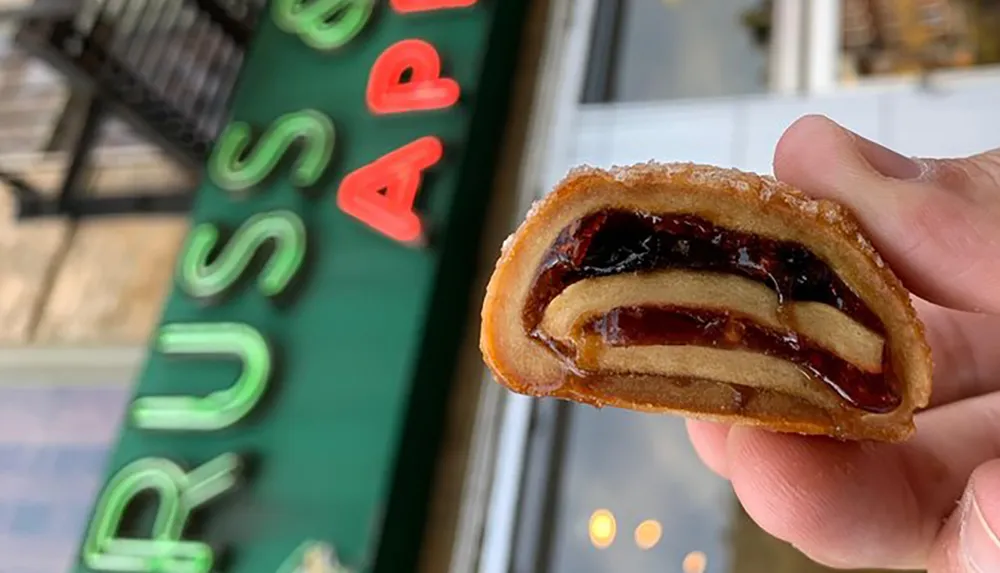 A person is holding a cross-section of a jelly-filled pastry with a blurred store sign in the background