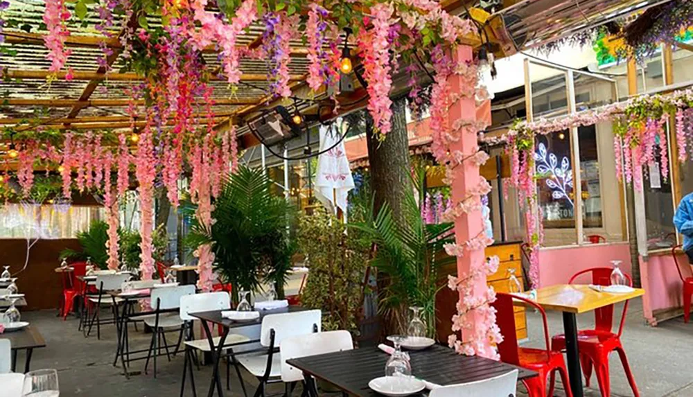 The image shows an outdoor restaurant patio adorned with pink artificial flowers providing a colorful and inviting ambiance for dining