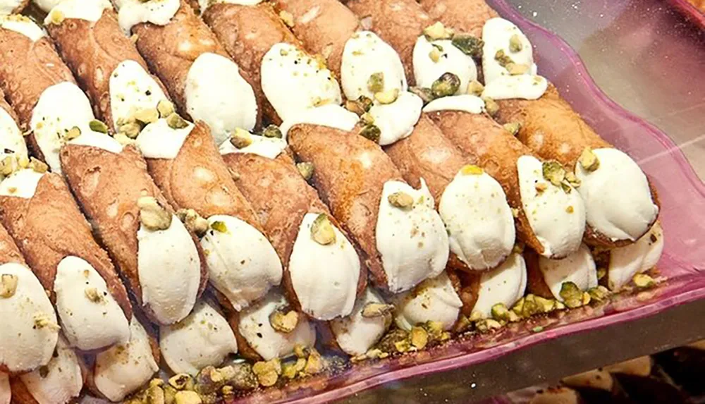 The image shows a tray of cannoli a traditional Italian dessert filled with a creamy white filling and topped with pistachios