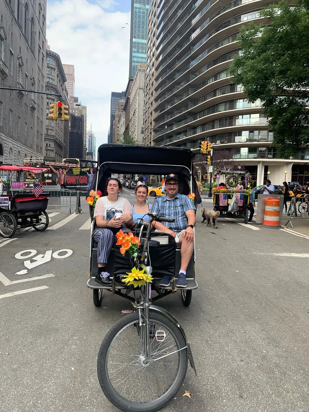 Three people are posing for a photo while seated on a pedicab adorned with flowers on a bustling city street