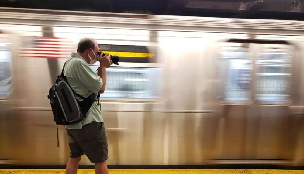 A person is taking a photograph with a DSLR camera while standing at a subway platform as a train blurs past