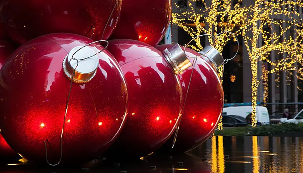This image shows oversized red Christmas ornaments with a backdrop of trees adorned in twinkling lights creating a festive holiday scene