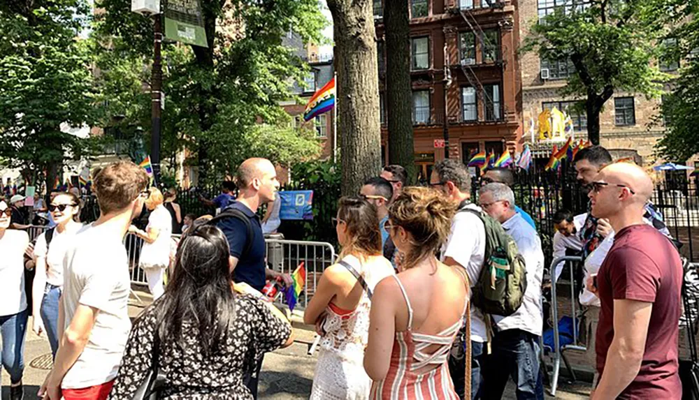 A diverse group of people gather at an outdoor event adorned with rainbow pride flags