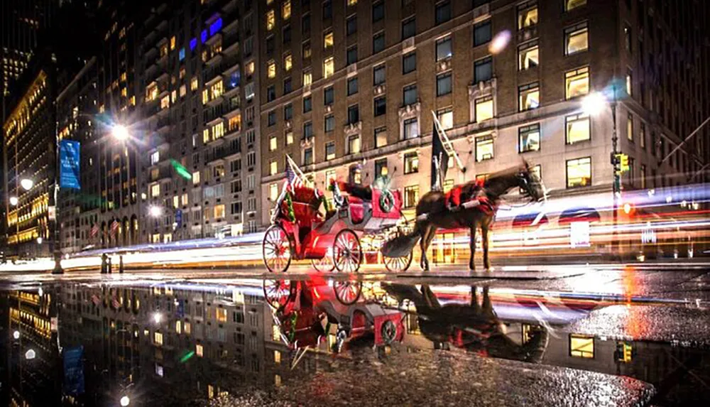 A red horse-drawn carriage stands on a wet city street at night with the lights of passing traffic creating a streaking effect as they reflect in the water on the ground