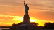 The Statue of Liberty is silhouetted against a vibrant sunset sky.