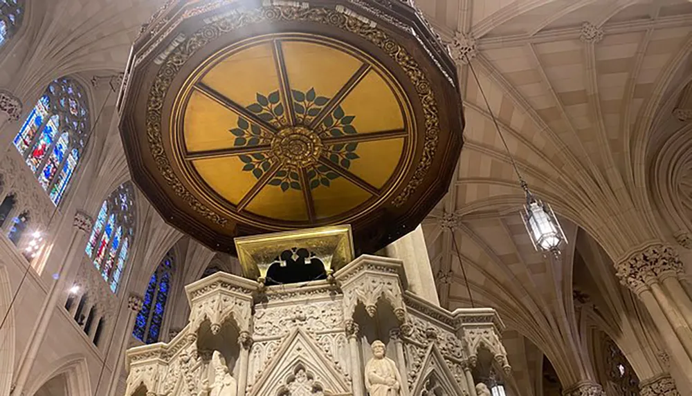 The image displays an ornate gold and maroon ceiling rose in a cathedral with Gothic architectural details and stained-glass windows