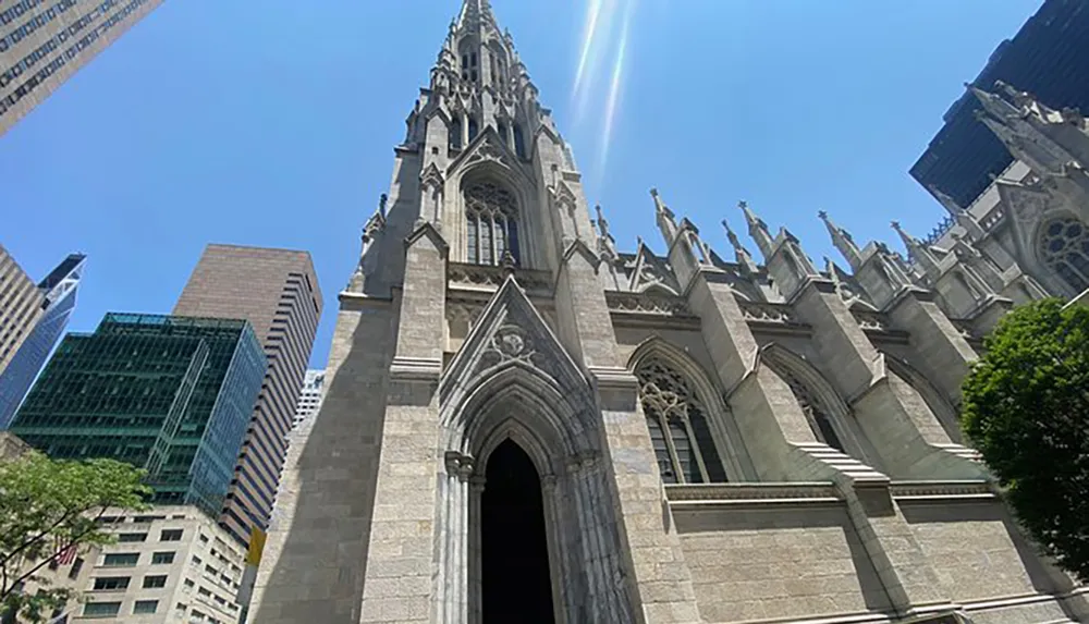 The image shows a Gothic-style cathedral with sharp arches and spires contrasting with the surrounding modern skyscrapers under a blue sky