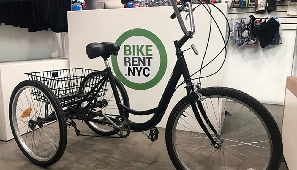 A black bicycle with a front basket is parked in front of a sign that reads BIKE RENT NYC suggesting a bike rental service location
