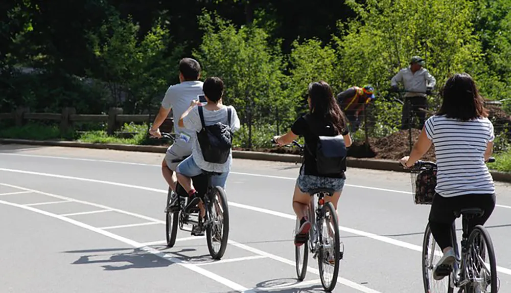 A group of people are riding bicycles on a sunny day sharing the road with a pedestrian in the background