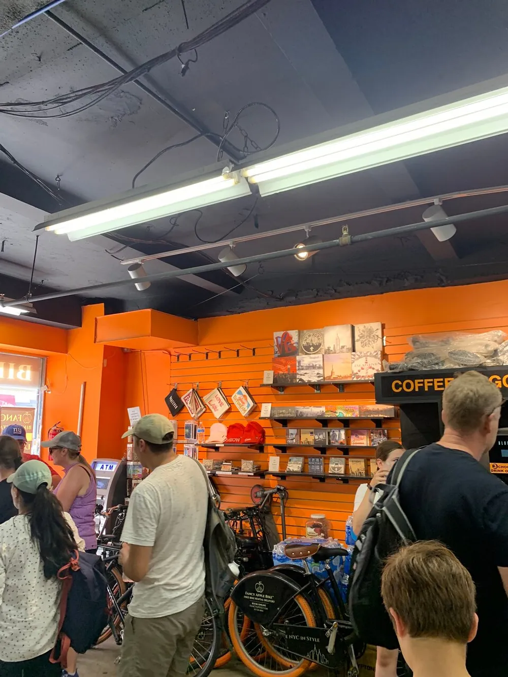 The image depicts a group of customers inside a store with bright orange shelves filled with merchandise and several bicycles parked amongst the shoppers suggesting a casual and possibly urban retail setting