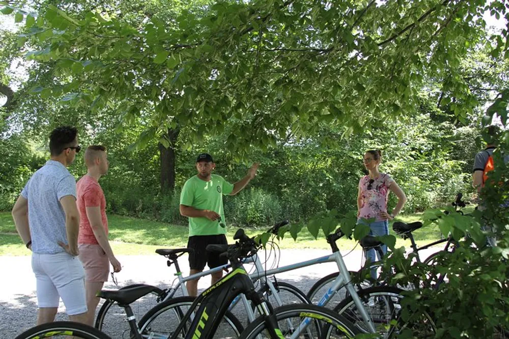 A group of people is standing near parked bicycles possibly engaged in a discussion or getting instructions from the individual gesturing with his hand
