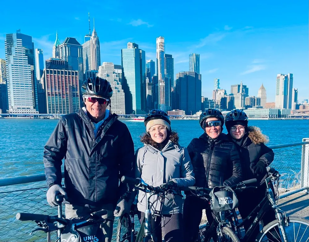 Four cyclists wearing helmets are posing for a photo with a city skyline in the background