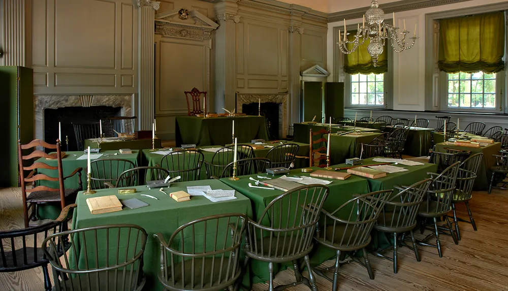 The image shows a historical room with green tablecloths wooden chairs and documents suggesting it is a carefully recreated setting from a significant past event