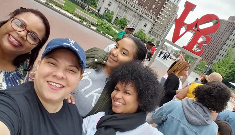 A group of people is taking a selfie in front of the iconic LOVE sculpture in a public space