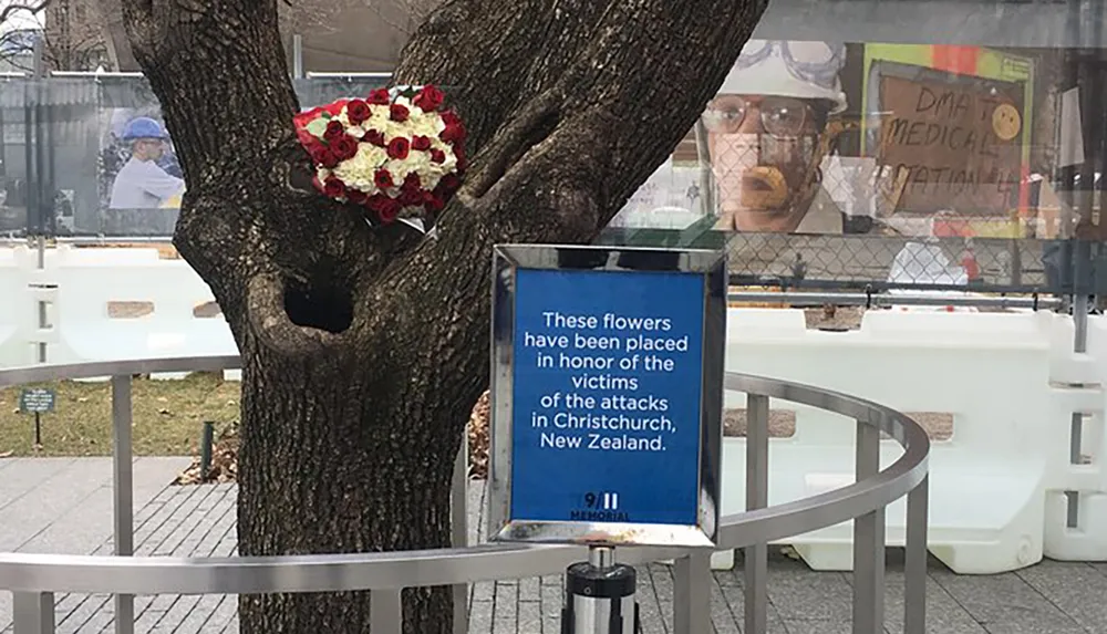 A heart-shaped floral arrangement is attached to a tree beside a sign indicating that the flowers honor the victims of the attacks in Christchurch New Zealand at the 911 Memorial