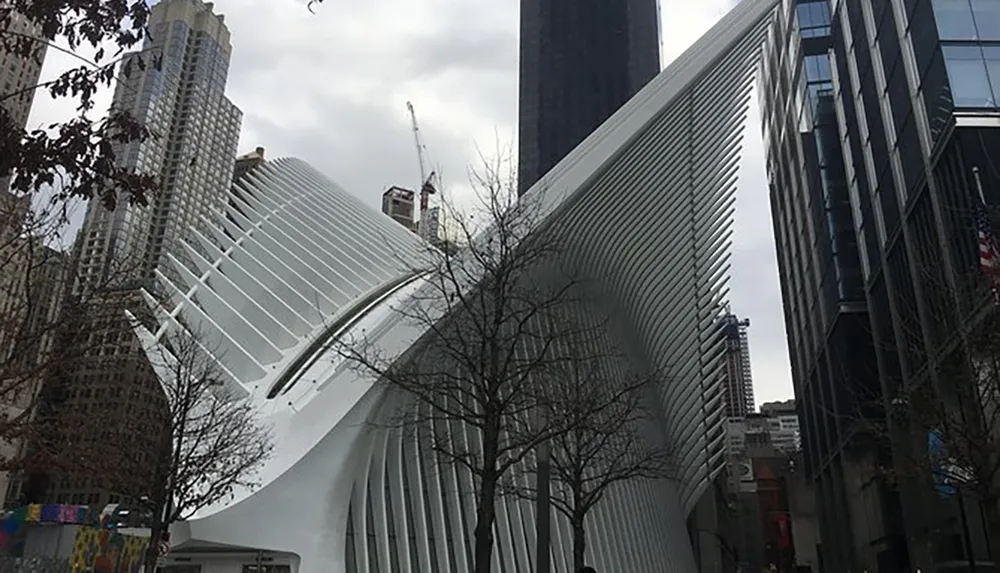 The image shows the unique modern architecture of the Oculus structure in New York City surrounded by skyscrapers on a cloudy day