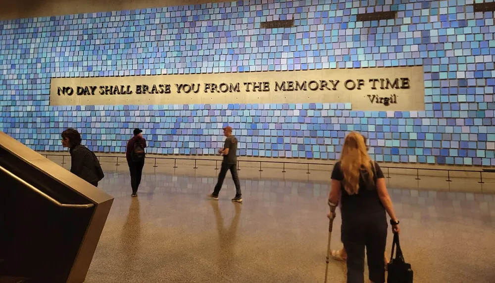 The image shows people walking past a wall with a mosaic and the Virgil quote No day shall erase you from the memory of time