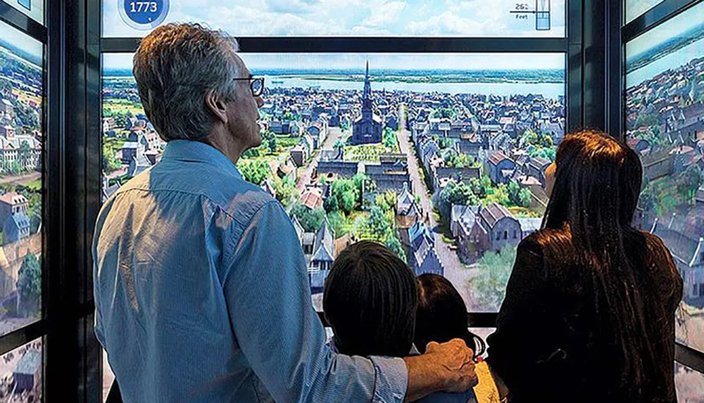 People are observing a panoramic view of a town displayed inside an elevator with a simulation screen