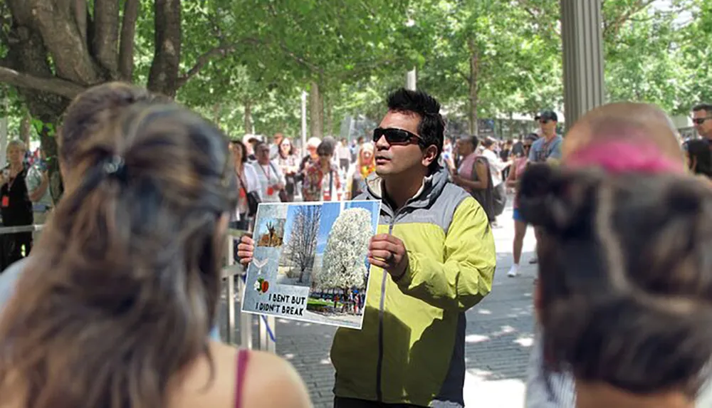 A person is holding up a poster with images of trees and text while standing outdoors in a crowd