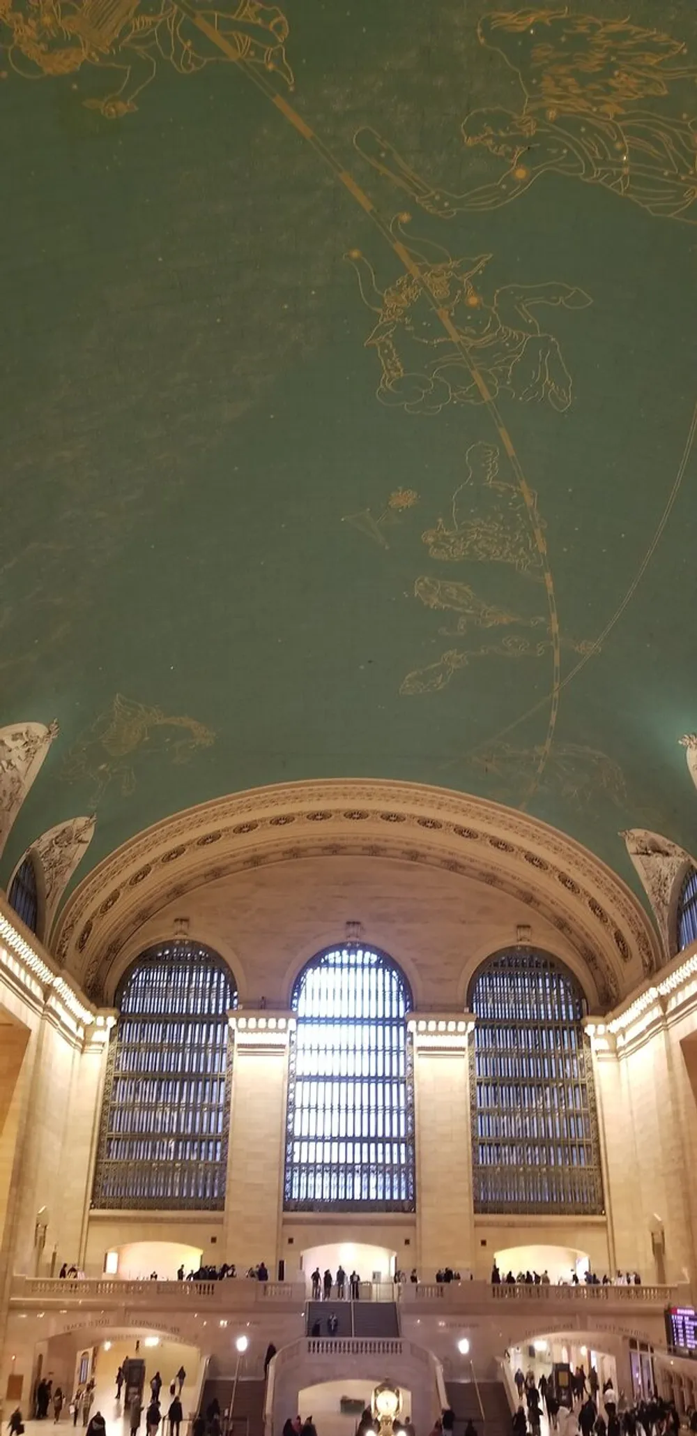 The image shows the interior of Grand Central Terminal in New York City with its spacious main concourse large arched windows and the iconic celestial ceiling mural