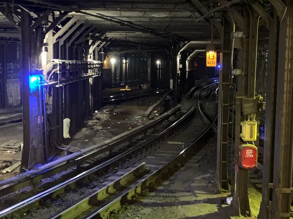 This is a dimly lit underground subway tunnel with tracks diverging and various signals and debris along the sides