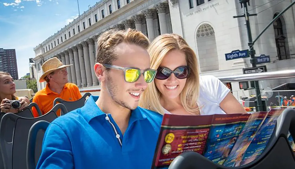 A couple is looking at a brochure together while on a sightseeing tour bus with other passengers and city buildings in the background