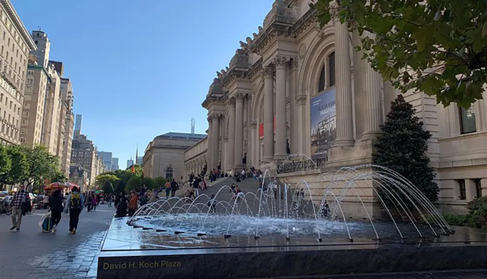 The image depicts a bustling scene outside the Metropolitan Museum of Art in New York City with people walking by and a fountain in the foreground