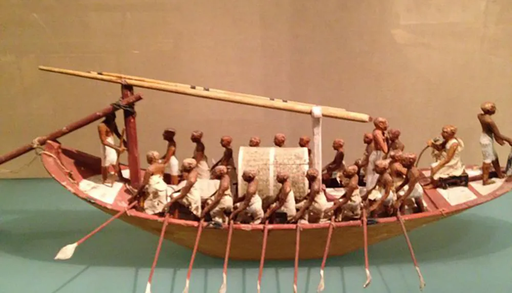 The image shows a detailed model of an ancient Egyptian funerary boat with figures rowing and performing various tasks