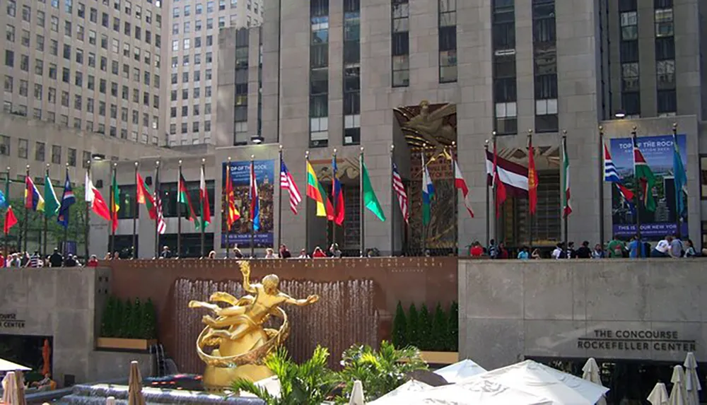 This image shows the iconic golden Prometheus statue overlooking the skating rink at Rockefeller Center surrounded by national flags