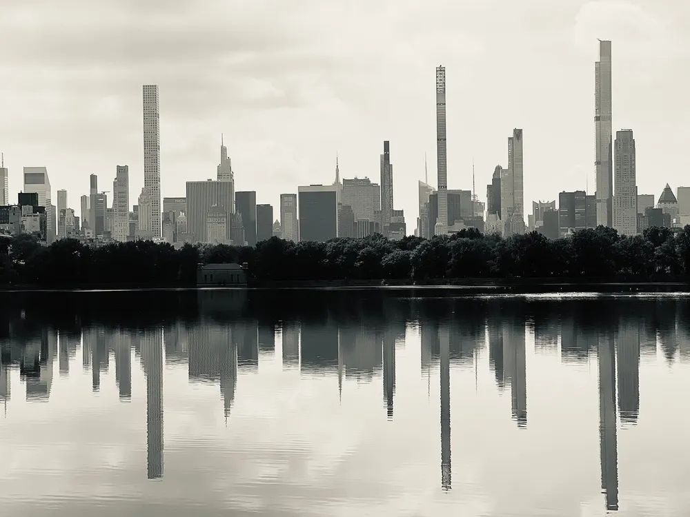 A monochromatic view of a city skyline with distinct skyscrapers reflecting over a calm body of water