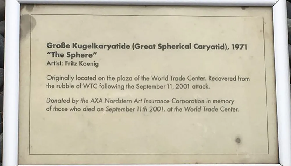 This image shows an informational plaque describing The Sphere a sculpture by Fritz Koenig that was originally located at the World Trade Center and later recovered from the rubble following the September 11 2001 attacks now donated by AXA Nordstern Art Insurance Corporation in memory of those who perished