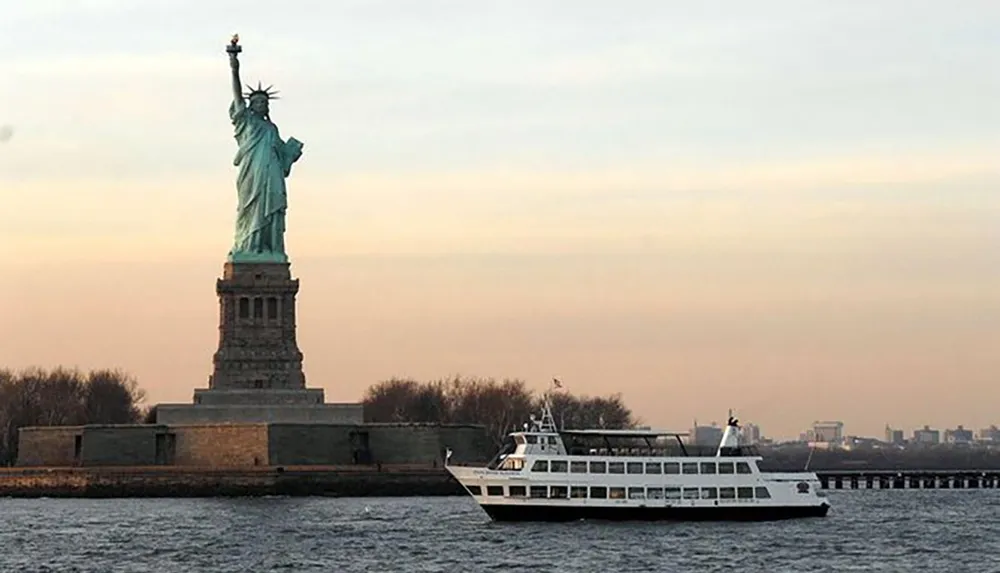 A ferry sails past the Statue of Liberty during what appears to be dusk or dawn