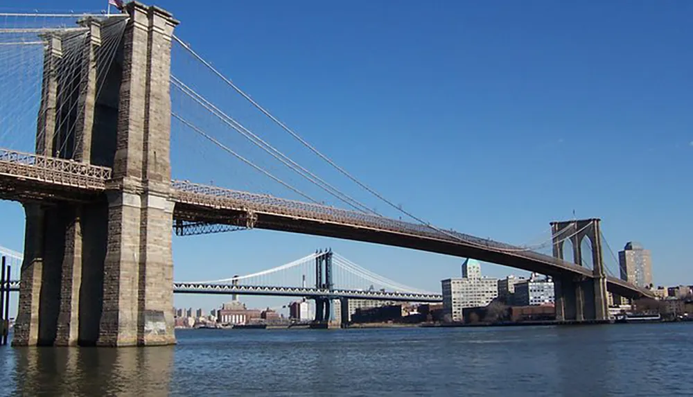 The image shows the Brooklyn Bridge an iconic suspension bridge spanning the East River between Manhattan and Brooklyn in New York City with the Manhattan Bridge in the background