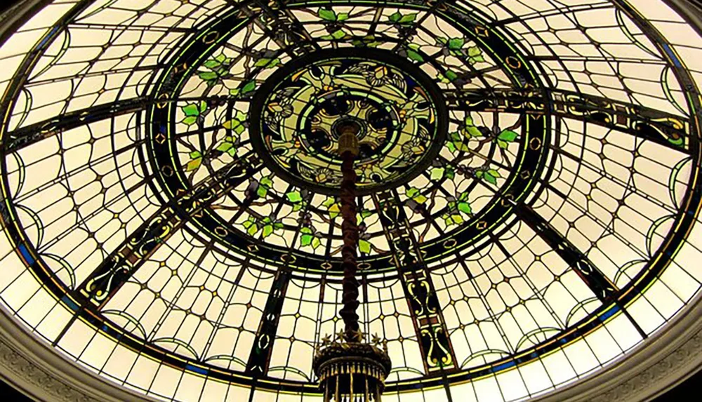 The image shows an ornate circular stained glass ceiling with a hanging chandelier viewed from below