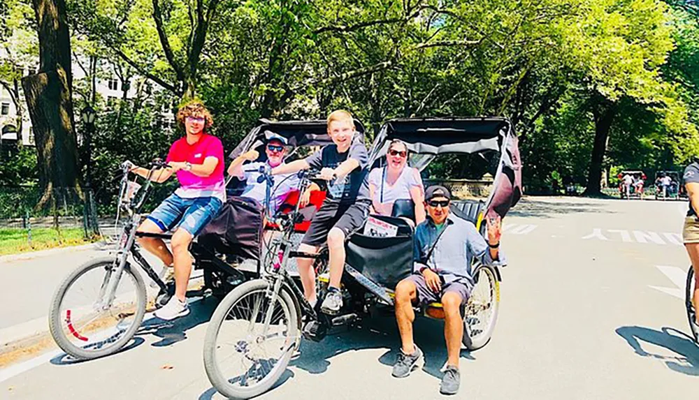 A group of people is posing for a photo with smiles on a pedal-powered vehicle likely a pedicab on a sunny day with trees in the background