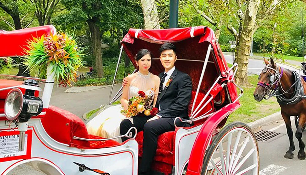 A couple dressed in formal attire is seated in a decorated horse-drawn carriage possibly celebrating a special occasion